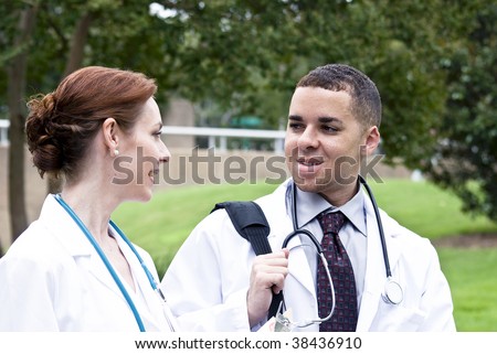 Two doctors on break in a city green space, engaged in friendly conversation.