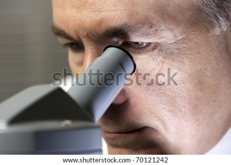 A close up of a doctor or scientist as he studies something through a microscope.
