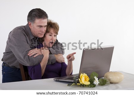 A mature couple read something the woman finds surprising on her laptop screen.