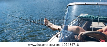 A man\'s leg rests on the side of a boat next to his fishing pole/Relaxing and Fishing/Fishing can be a relaxing day