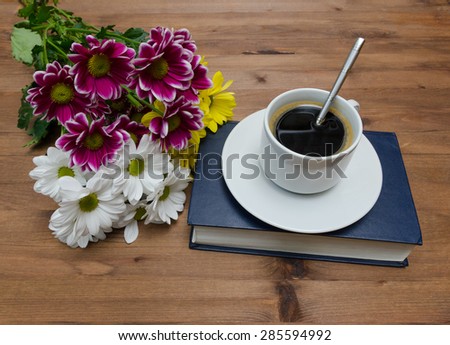 Cup of coffee with flowers and book on old wooden table