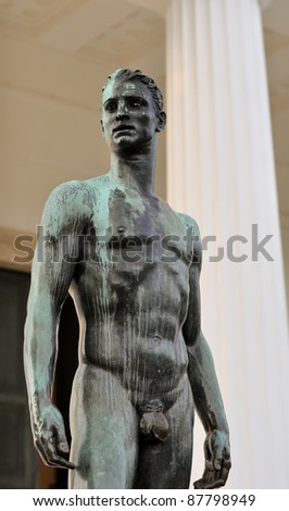 athletic male bronze statue with a longing stare in front of greek columns