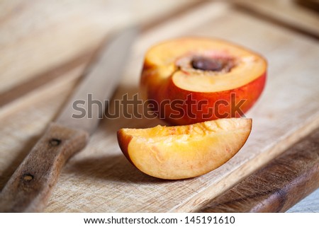 Sliced peach and knife placed on wooden plate.