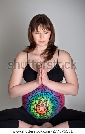 Pregnant woman with painted belly doing yoga exercise