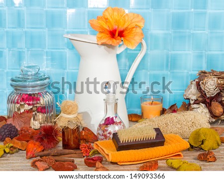 Exotic spa bathing accessories with an orange hibiscus flower in a jug against turquoise blue tiles with rose petal potpourri , bath salts, sponges and a variety of luxury bathing accessories