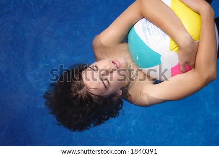 Teenage boy floating on his back in swimming pool while holding onto a beach ball