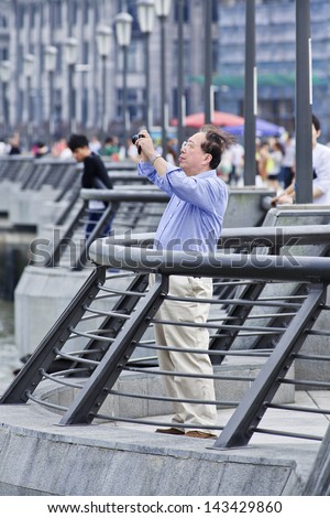 SHANGHAI-JUNE 6. Old Chinese man photographing at The Bund. It is a waterfront area, central Shanghai, which runs along the western bank of Huangpu River, facing Pudong area. Shanghai, June 6, 2013.