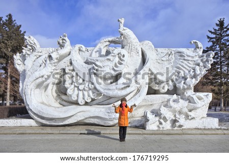 CHANGCHUN, CHINA - FEB. 3, 2014. Girl poses in front of snow sculpture in Nanhu Park Changchun, capital of northeast Jilin Province. Traditionally every year are snow sculptures exhibited in Nanhu park.