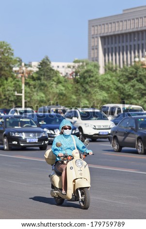 BEIJING-MAY 29, 2013. Chinese woman with mouth cap on e-bike. The US Embassy measures the Beijing air often as very unhealthy and even hazardous; smog protection has become a familiar phenomenon.