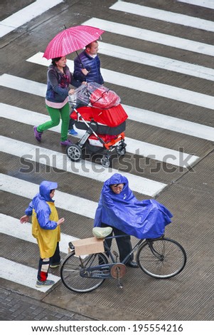 SHANGHAI-MAY 4, 2014. People with umbrella and rain-wear on wet zebra path. Shanghai has a humid subtropical climate, its summer is warm and humid, with occasional downpours or freak thunderstorms.