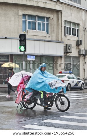 SHANGHAI-MAY 4, 2014. Father and son dressed in rain-wear on an e-bike. Shanghai has a humid subtropical climate, its summer is very warm and humid, with occasional downpours or freak thunderstorms.