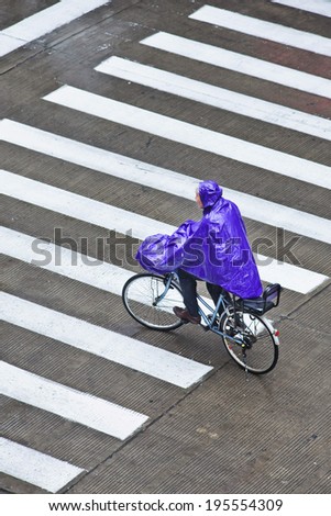 SHANGHAI-MAY 4, 2014. Cyclist dressed in rain-wear on a wet zebra path. Shanghai has a humid subtropical climate, its summer is very warm and humid, with occasional downpours or freak thunderstorms.