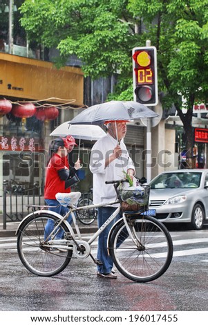 SHANGHAI-MAY 4, 2014. Chinese elderly with bicycle and umbrella on a rainy street. Shanghai has humid subtropical climate, its summer is warm and humid, with occasional downpours or thunderstorms.