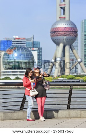 SHANGHAI-MAY 5, 2014. Girls with smart phone makes selfie with Pudong on background. Pudong district houses Lujiazui Finance and Trade Zone and Shanghai Stock Exchange, it is China\'s financial center.