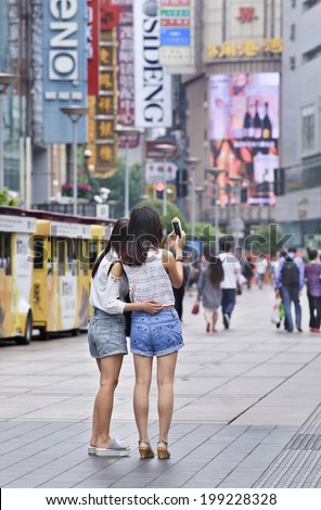 SHANGHAI-JUNE 4, 2014. Girls in Nanjing East Shopping Street take a photo with their smart phone. It is the main shopping street of Shanghai, and also one of the world\'s busiest shopping streets.