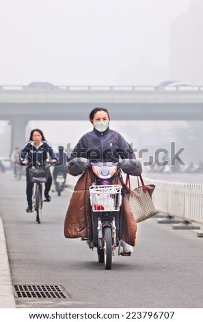 BEIJING-OCT. 11 ,2014. Woman on e-bike in smog blanketed city. A concentration of PM2.5, small particles that poses a huge health risk, hit 462 according U.S. Embassy pollution monitor in Beijing.