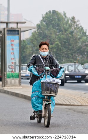BEIJING-OCT. 19, 2014. Woman with mout cap on an e-bike. Beijing raised its smog alert to orange because the air quality is a health threat. Face masks, once a rarity in Beijing, have become common.