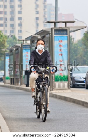 BEIJING-OCT. 19, 2014. Woman on a bicycle with face mask. Beijing raised its smog alert to orange because the air quality is a health threat. Face masks, once a rarity in Beijing, have become common.