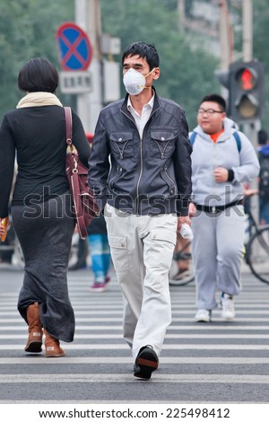 BEIJING-OCT. 19, 2014. Face masked man on a zebra path. Beijing raised its smog alert to orange because the air quality is a health threat. Face masks, once a rarity in Beijing, have become common.