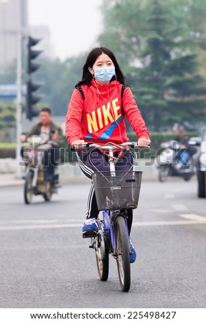 BEIJING-OCT. 19 ,2014. Face-masked cyclist in smog blanketed city. Beijing raised smog alert to orange because the air quality (concentration of PM2.5 small particles) became a human health threat.
