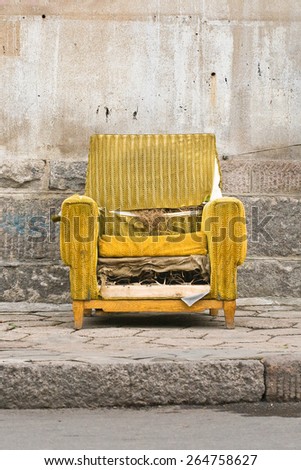 Old worn out yellow chair against a stone wall