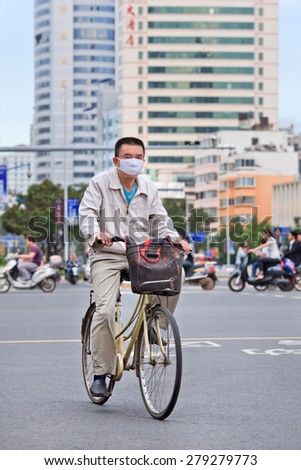 KUNMING-JUNE 30, 2014. Man with mouth cap on bicycle. An increasing number of Chinese citizens wear breath protection, only eight out of China\'s 74 biggest cities passed 2014 air quality standards.