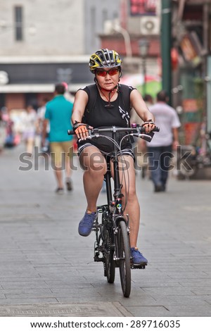 BEIJING, CHINA -JUNE 9, 2015. Sporty middle-aged woman rides her bike. Three decades ago the main transport mode in Beijing was people\'s bicycle. Nowadays many citizens buy bicycles only for leisure or sport activities.