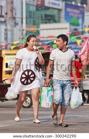 BEIJING-JULY 24, 2015. Husband carries stuff, fat woman eats ice-cream. China\'s obesity rate has skyrocketed over last decades, resulting in 46 million obese Chinese adults and 300 million overweight.