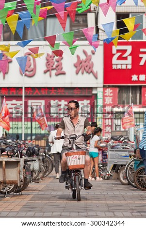 BEIJING-JULY 24, 2015. Man on e-bike in shopping area. In a decade, e-bikes in China climbed from near zero to 150 million (2015), the largest adoption of alternative fuel vehicle motorization history
