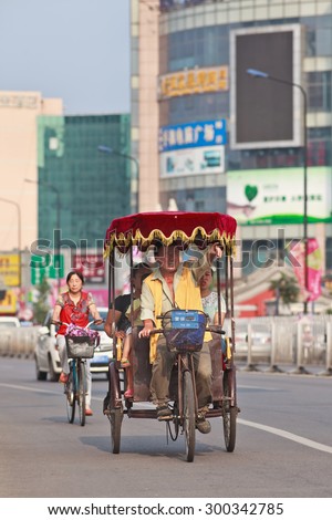 BEIJING-JULY 24, 2015. Cheerful rickshaw driver with passengers. In Chinese cities rickshaws are still a popular and affordable transport mode for short distances, cost is lower than a regular taxi.