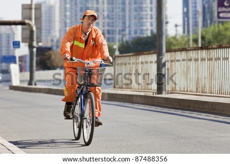BEIJING - OCT. 25: Worker in orange cycles in Beijing, Oct. 25, 2011. From 1995 to 2005, China\'s bike fleet declined by 35 percent and private car ownership more than doubled.