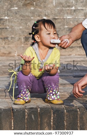 PINGYAO-CHINA-SEPT.6, 2006. unidentified Child eats ice-cream out of fathers hand on Sept. 6, 2006 in Pingyao. Because of China\'s one-child policy (since 1979) families can have only one child or risk steep fines.