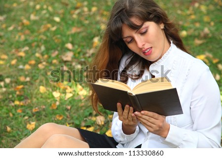 Reading on the nature.The girl reads the book, sitting on a green grass. It is dressed in a white blouse and a black skirt.