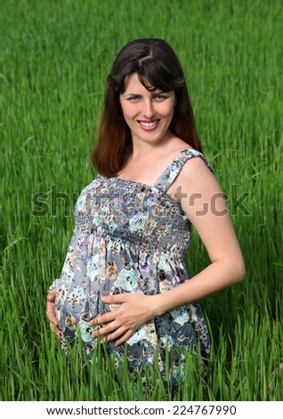 Pregnancy. Happy future mother hugs her belly with his hands against the green grass.