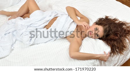 Sexy and stunning young brunette woman laying on bed with only a white sheet covering her body