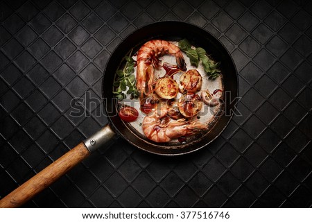 King-size shrimps and 3 scallops on a old black pan. Top view.