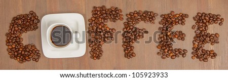 The word Coffee spelled with hundreds of coffee beans and one cup of coffee, isolated against wooden background