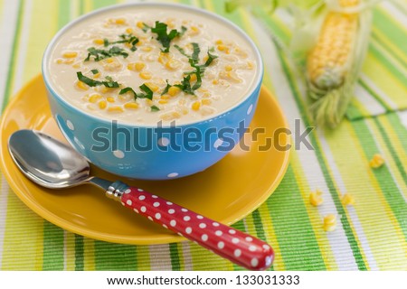 Cream of corn soup in blue bowl with fresh cob of corn on the side