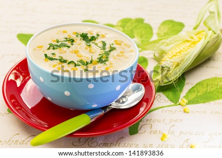 Cream of corn soup in blue bowl with fresh cob of corn on the side