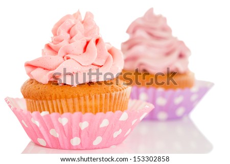 Two cupcakes in pink and purple polka dot cups, isolated on white background