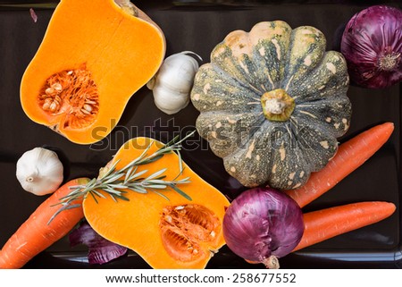 Pumpkin, carrot, onion, garlic and rosemary on black tray ready to roast