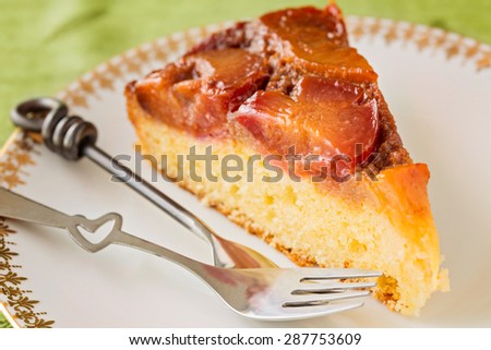 Slice of homemade upside-down plum cake with two forks in white plate, close up, horizontal composition