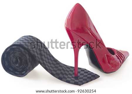 Red stiletto shoe standing on black rolled tie, concept of control, isolated on white background