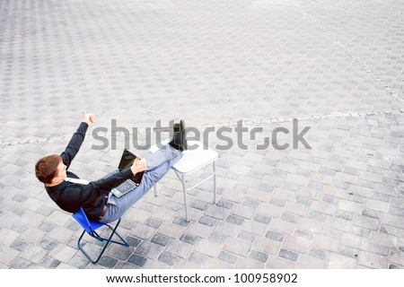 The image on top of a businessman sitting at the table in the street, which works with the computer and has a success.