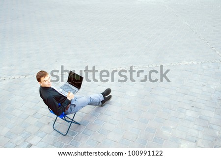 The image of a businessman sitting at the table in the street, which works with the computer and has a success.