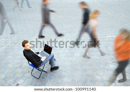 The image of a businessman working on the computer and sitting in the middle of people at the street