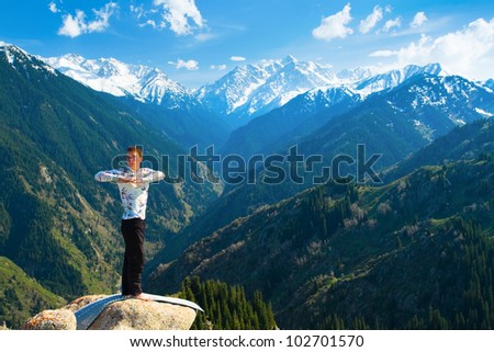 The young man is doing yoga warm-up before the yoga asanas on the summit. On the background is a range of high tops of mountains.