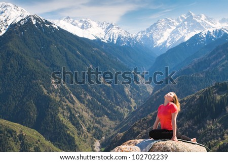 The young woman is doing a yoga asana Ã?Â¢??Pose of pigeonÃ?Â¢?Ã?Â� on the summit. On the background is a range of high tops of mountains.