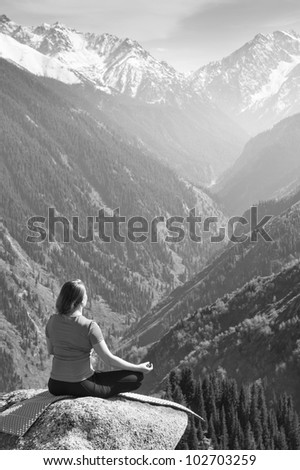 Black and white image, in which a young woman meditating on a mountain on the background of a very beautiful valley.