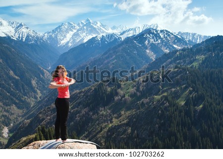 The young woman is doing yoga warm-up before the yoga asanas on the summit. On the background is a range of high tops of mountains.